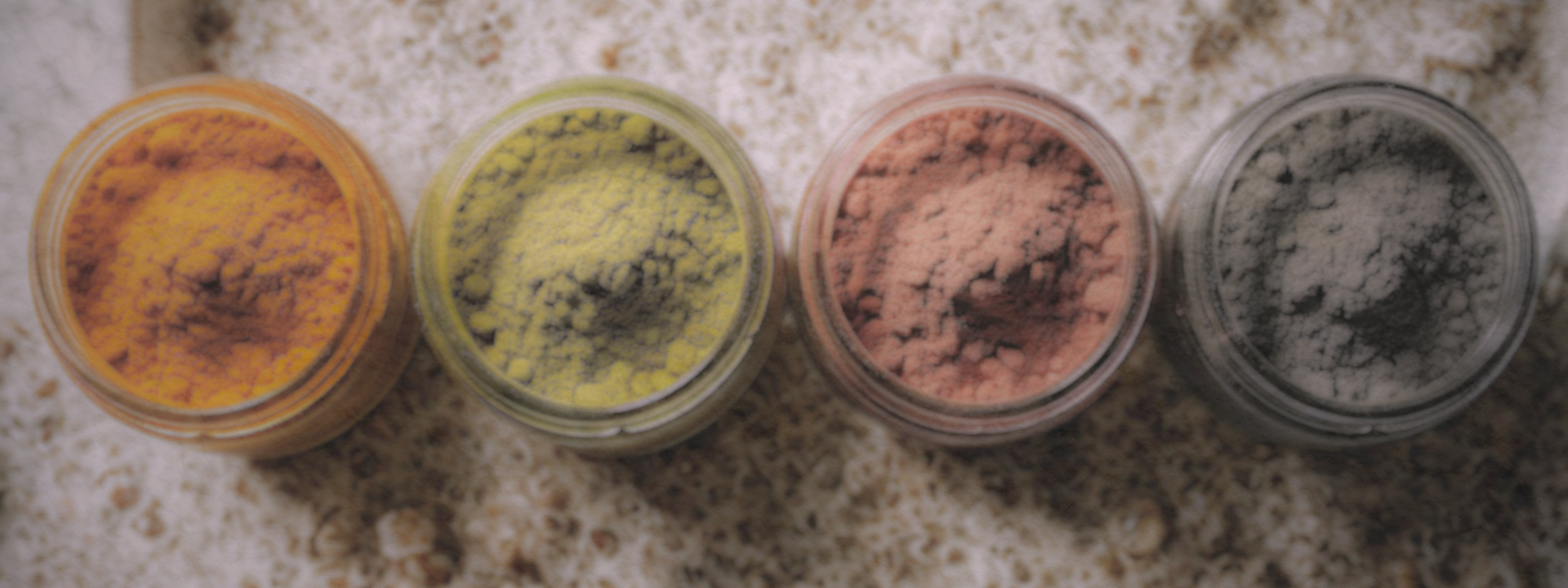 Four small jars with colorful powders on a textured surface